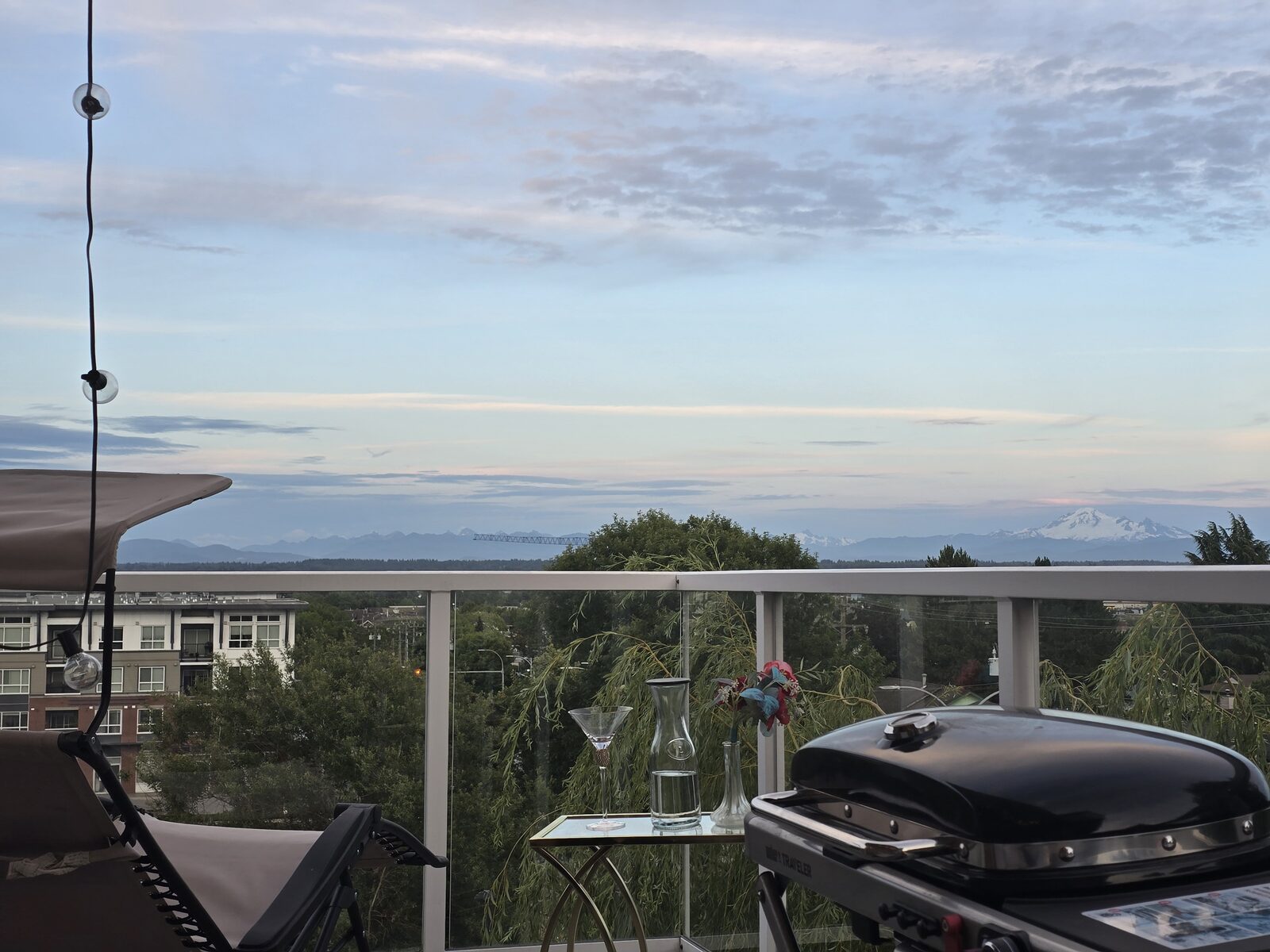 Wicker lounger, reclining chair, side table and portable BBQ on the balcony with mountain view