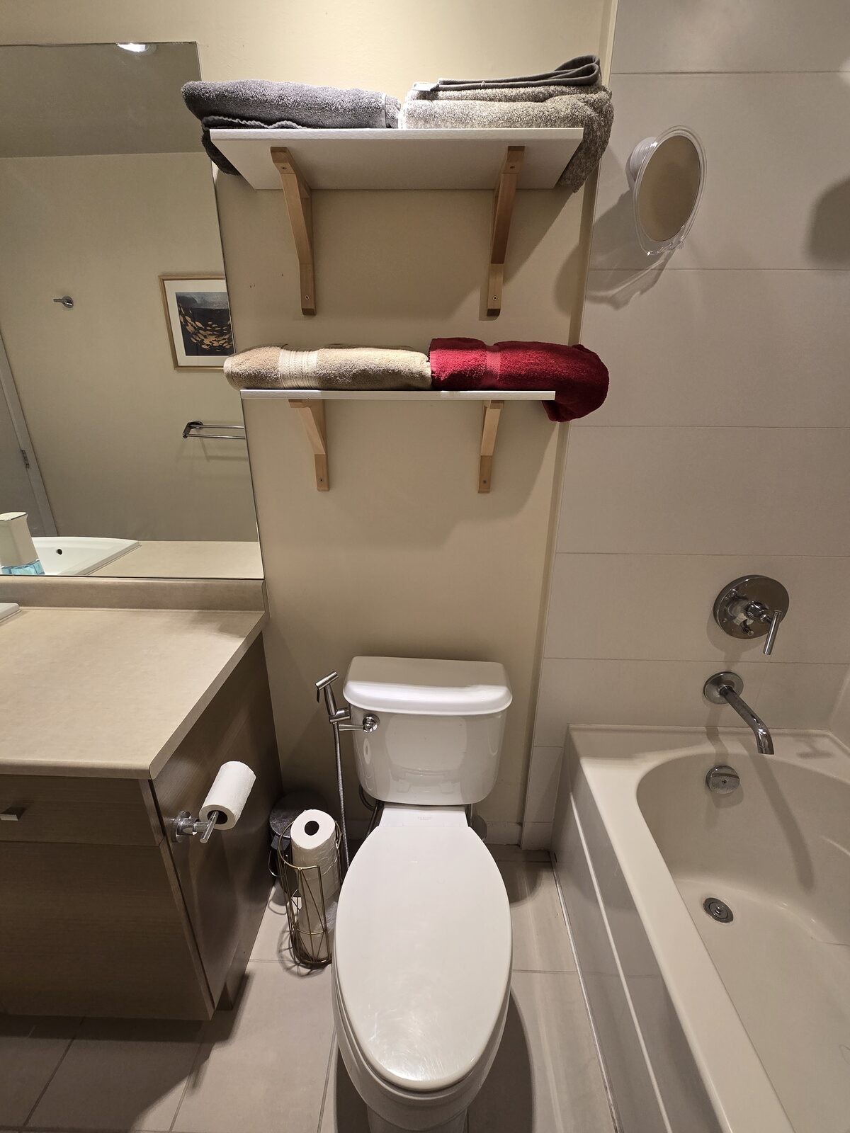 Toilet with euro-style handheld bidet sprayer and folded towels on shelving above