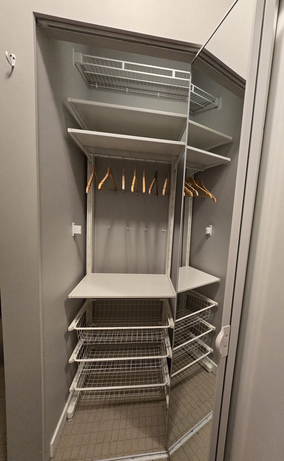 First bedroom closet with evenly spaced wood hangers and wire storage baskets