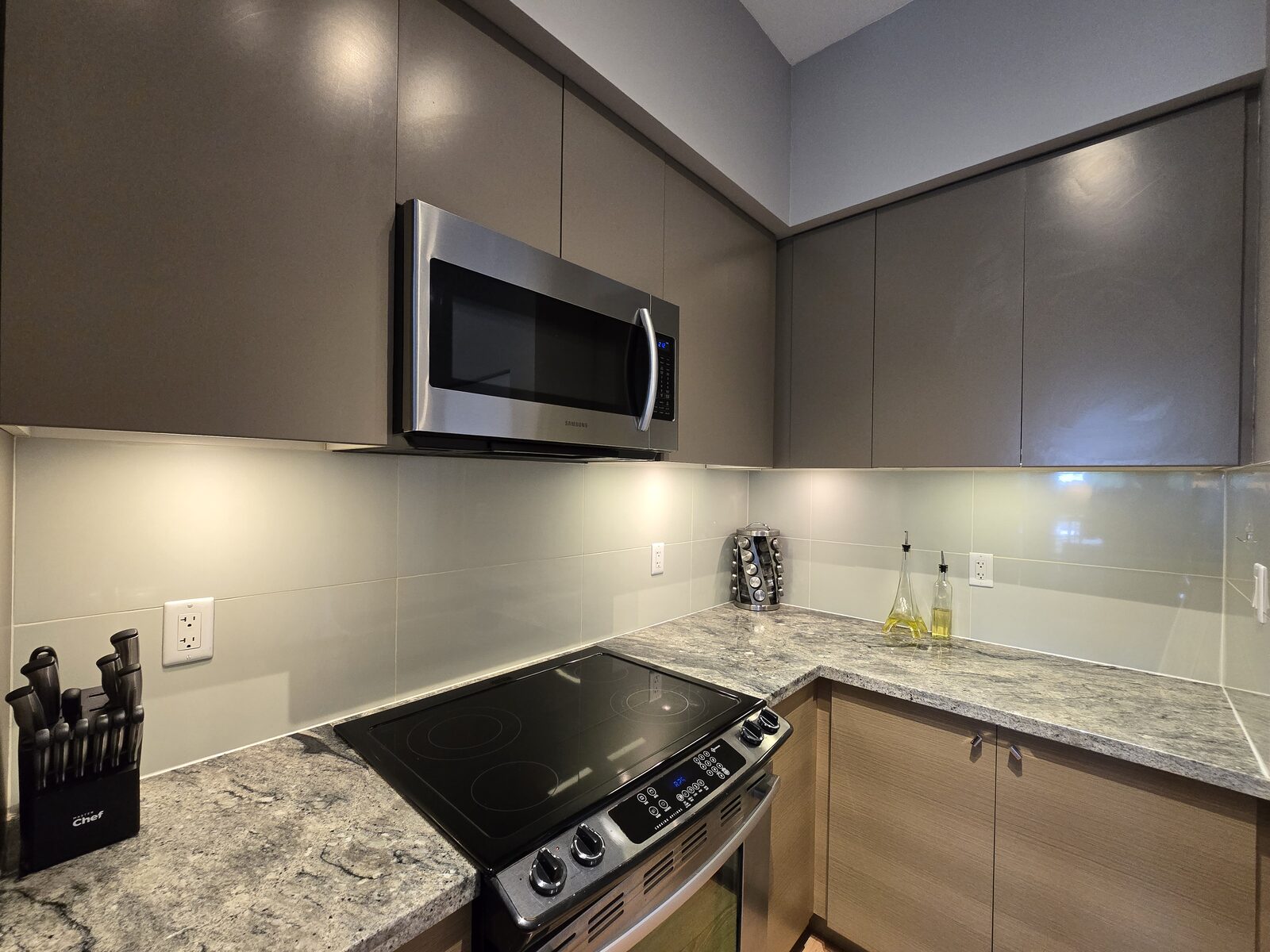 Corner counter with glass-top range, microwave, and granite backsplash