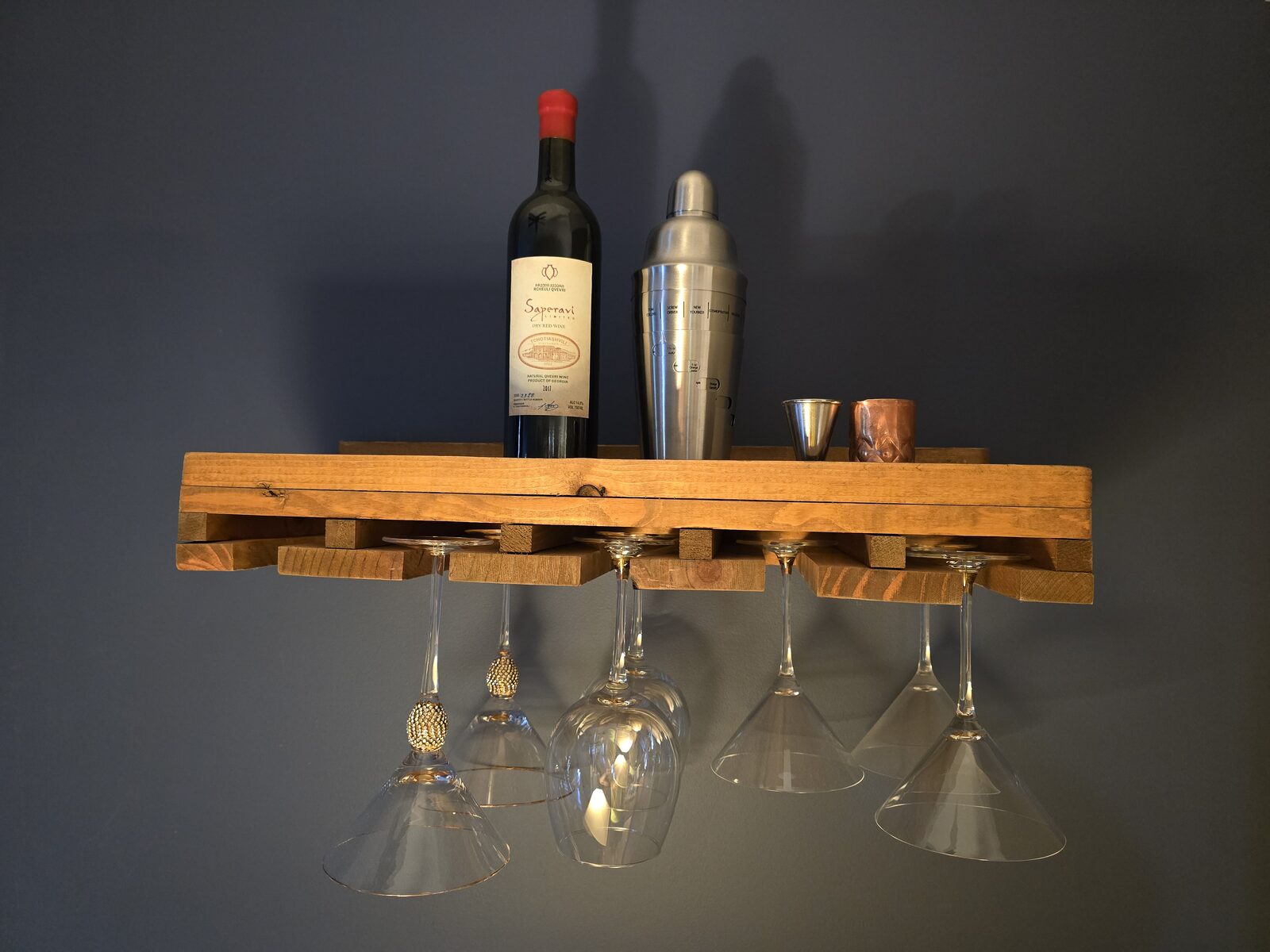Wall-mounted wine bar shelf with wine bottle, cocktail shaker, and hanging wine glasses